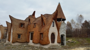 Casa cu acoperișuri ondulate și turn, construită din materiale naturale.