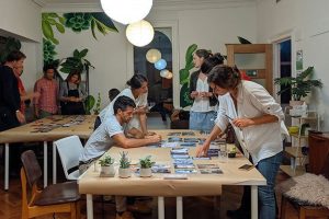 Oameni discutând și lucrând la un colaj creativ într-un spațiu plin de plante.
