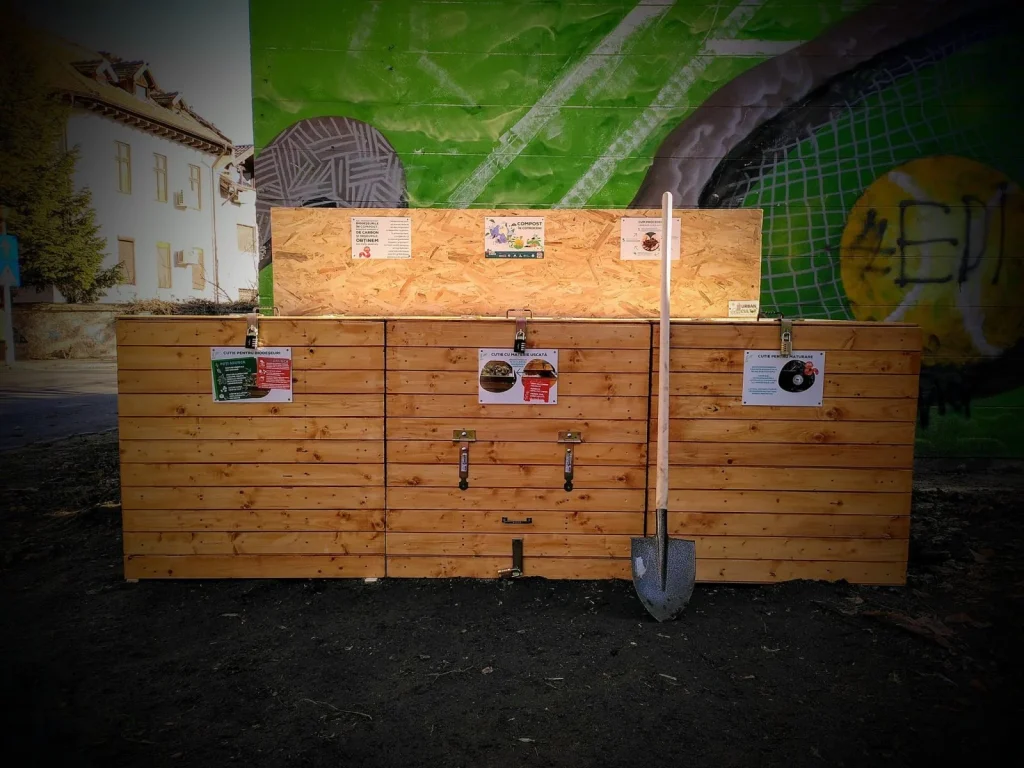 Compost café with wooden bins and a shovel, in front of a green mural.