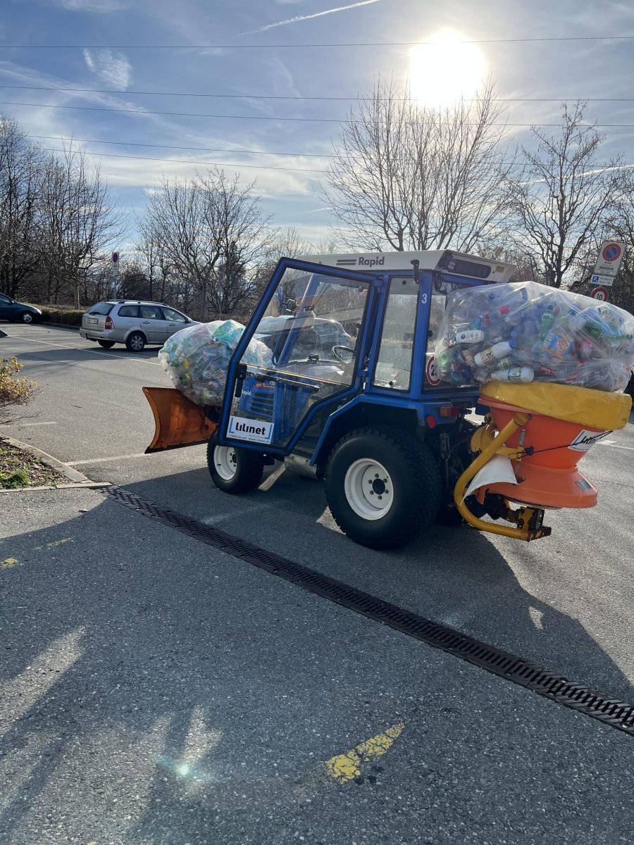 A specialized waste collection vehicle filled with plastic, set against an urban landscape.