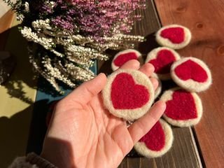 Mărțișoare ecologice din lână, cu inimă roșie, pe o masă de lemn.