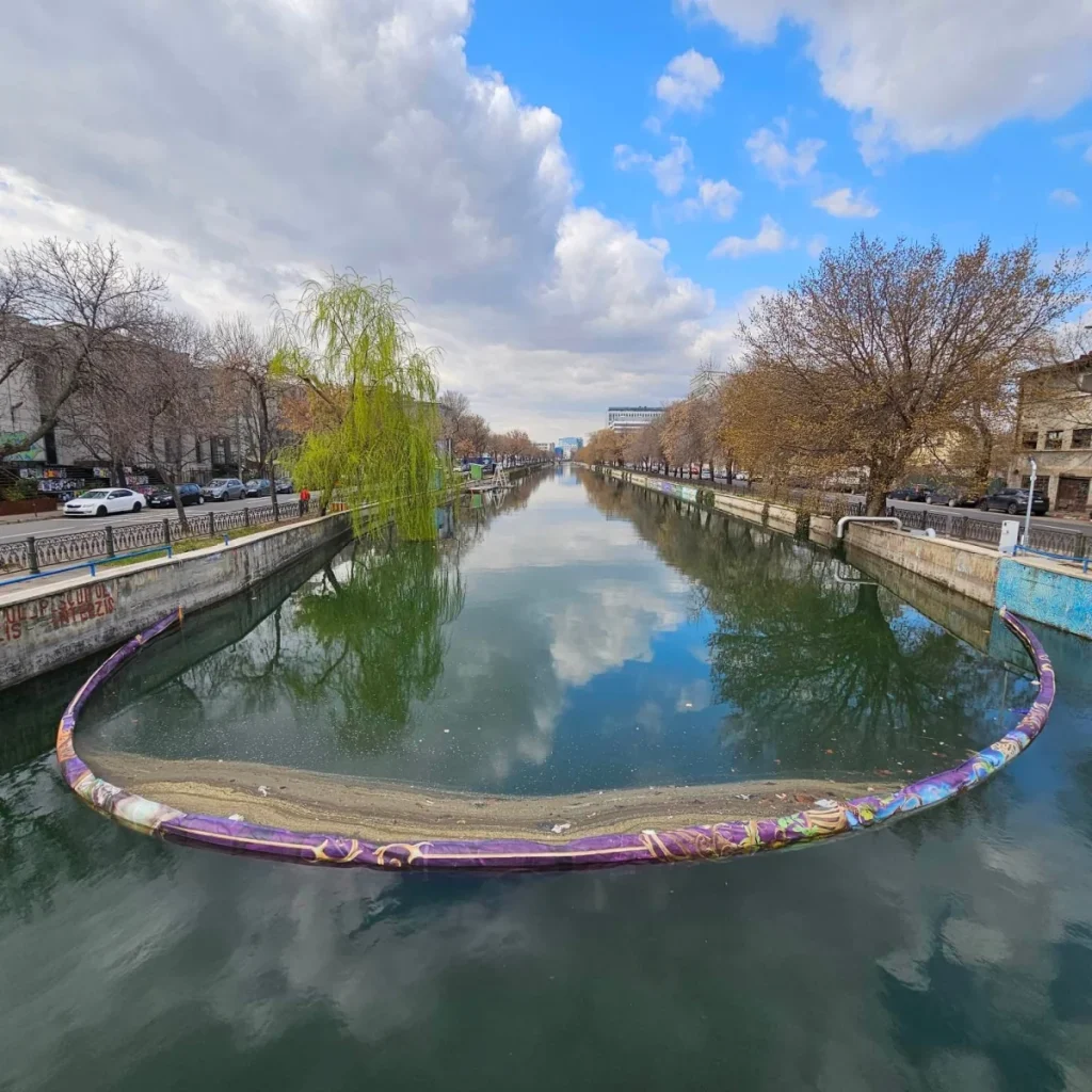 Floating barrier on Dâmbovița River capturing waste and debris.