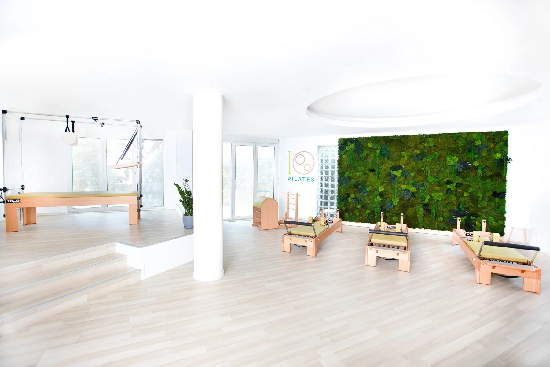 Studio de Pilates modern, cu echipamente de Pilates și un perete verde cu plante.