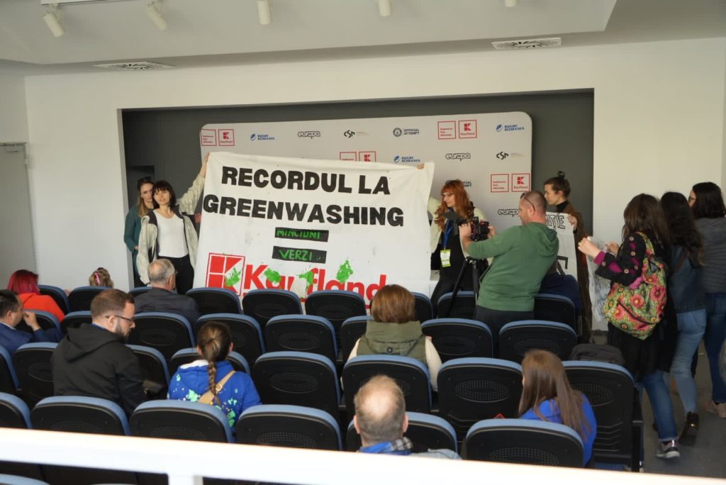 Protest against Kaufland's greenwashing, featuring a large banner in front of the audience.