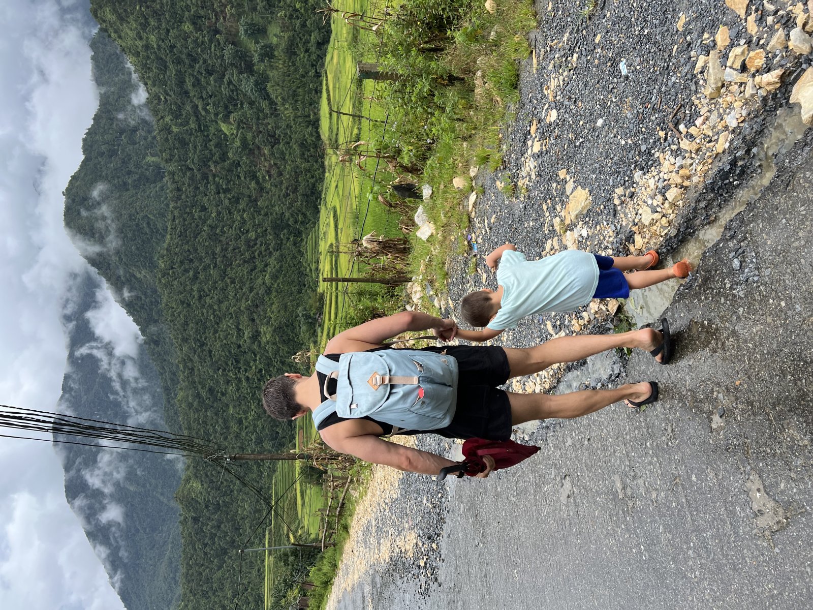 A family walks along a rural road in Vietnam, surrounded by lush green mountain scenery.