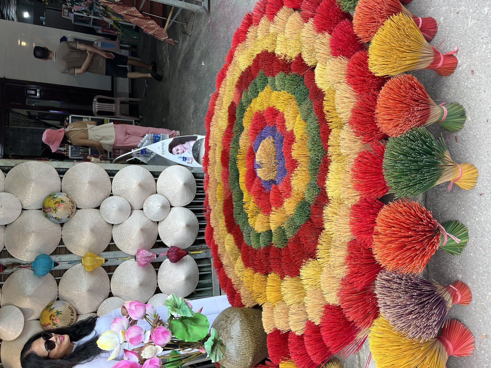A colorful mat made of wooden sticks and a woman with flowers, traditional Vietnamese hats in the background.
