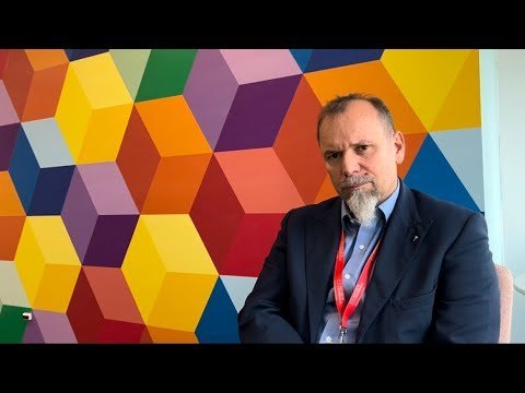 A man in a suit sits in front of a colorful wall, discussing the NET ZERO goal.