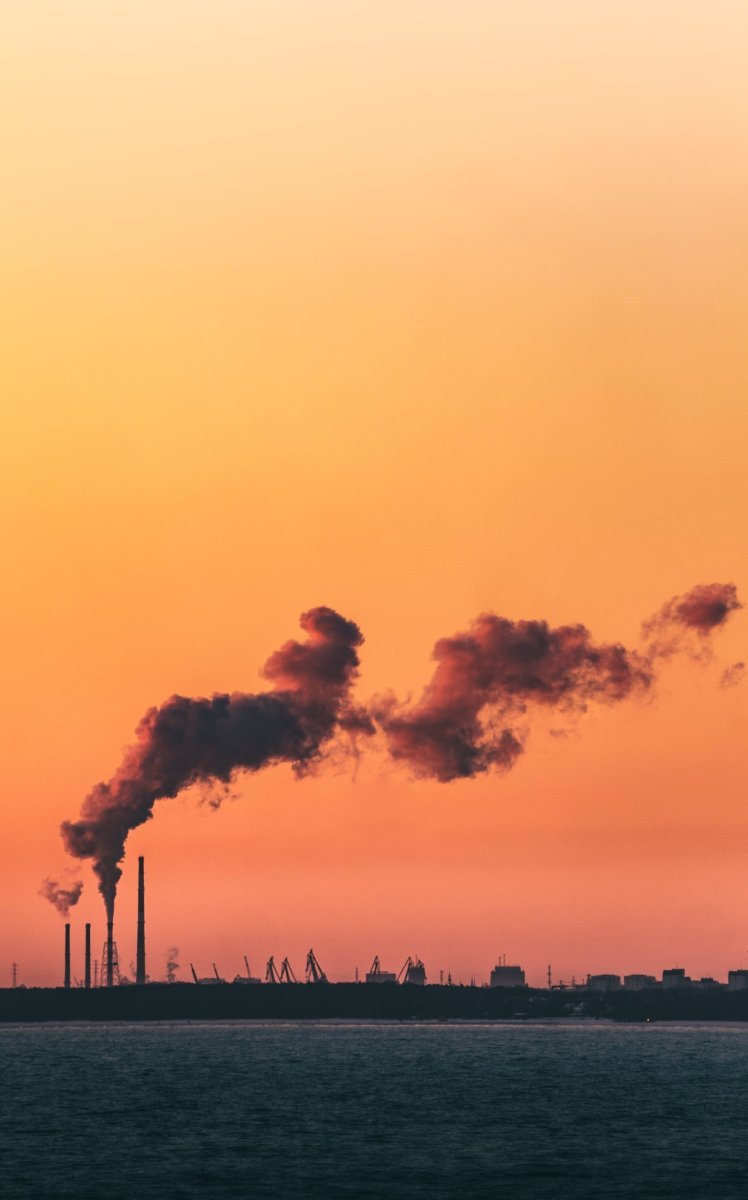 Thick smoke from a polluting factory against a sunset backdrop.