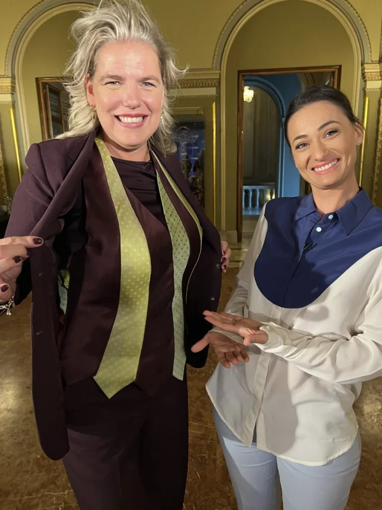 Two smiling women, one in a purple suit with a green tie, the other in a white and blue blouse.