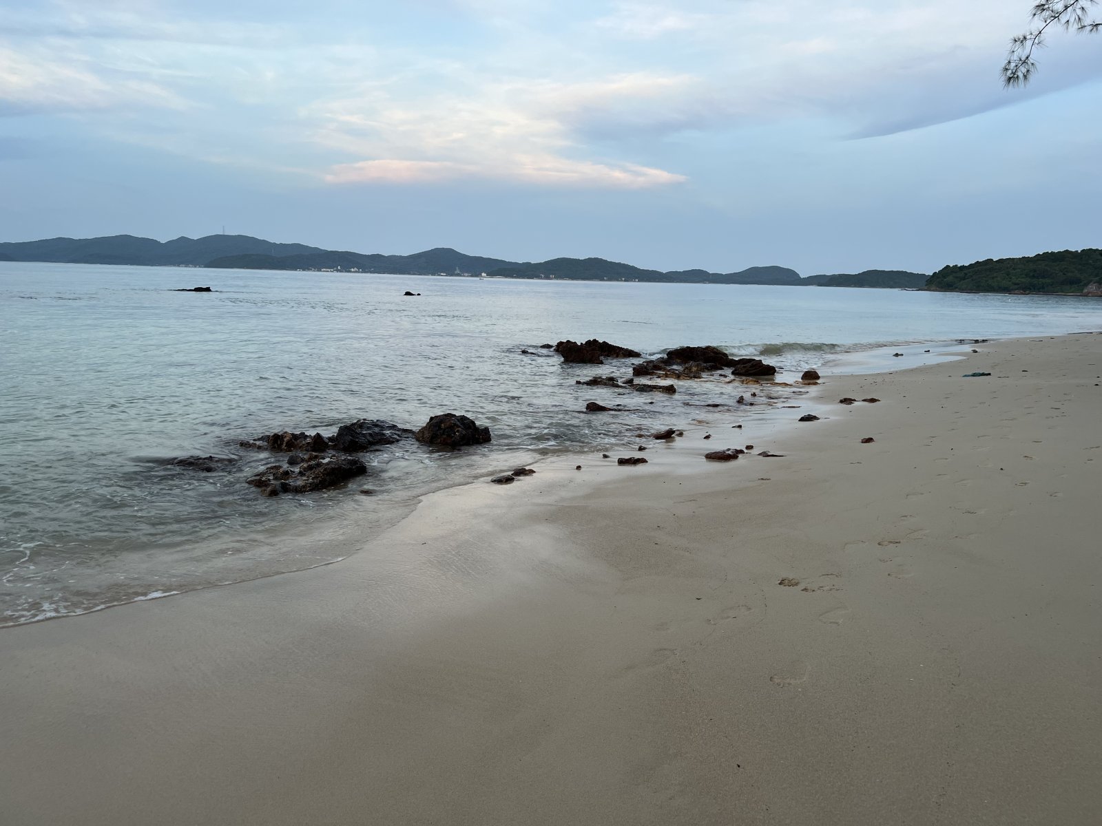 Sandy beach with clear water, rocky shore, serene natural landscape.