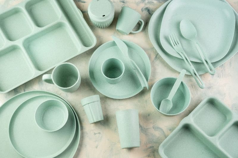 Reusable tableware in green shades, including plates, cups, and utensils.