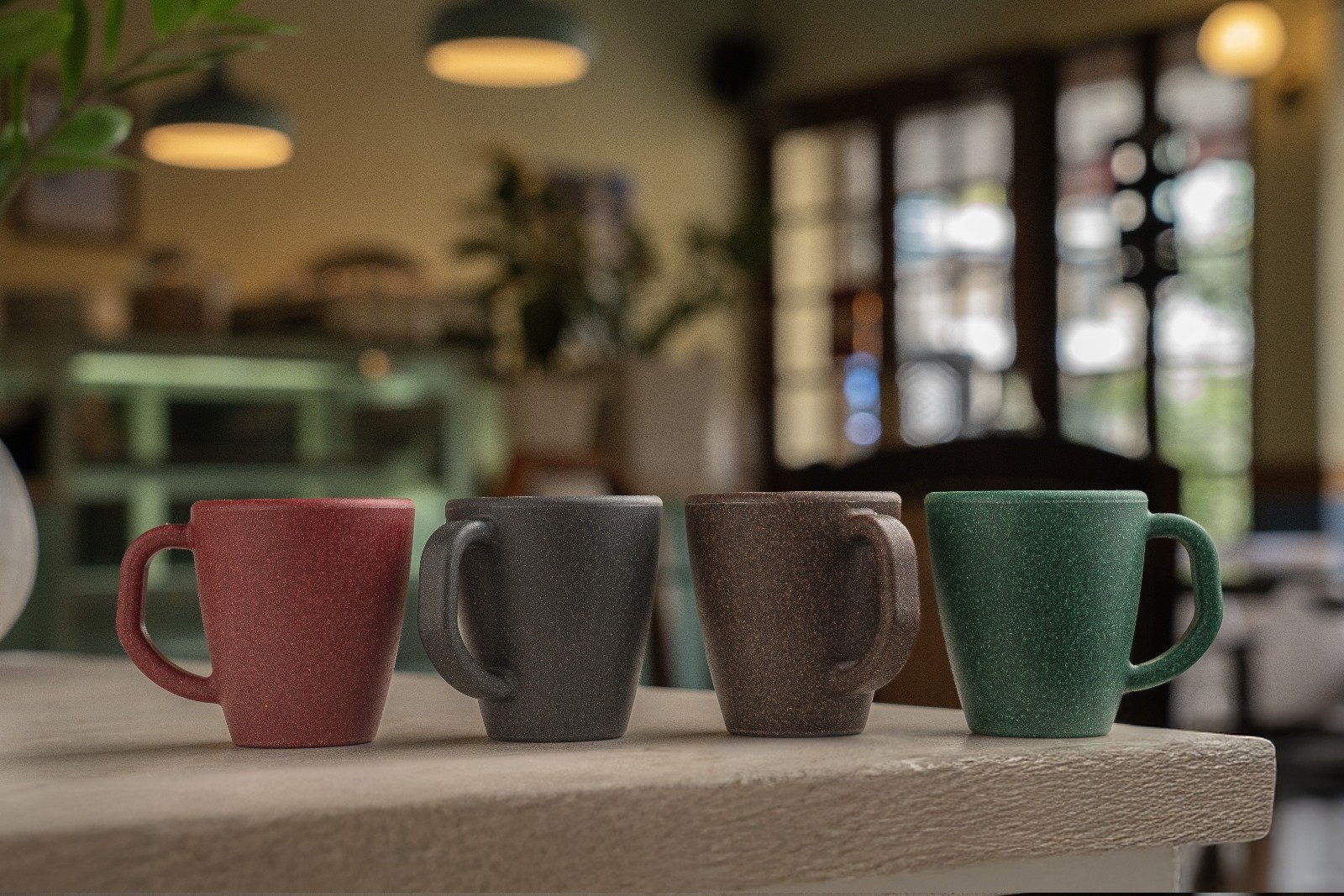 Five reusable cups in various colors on a table in a restaurant.