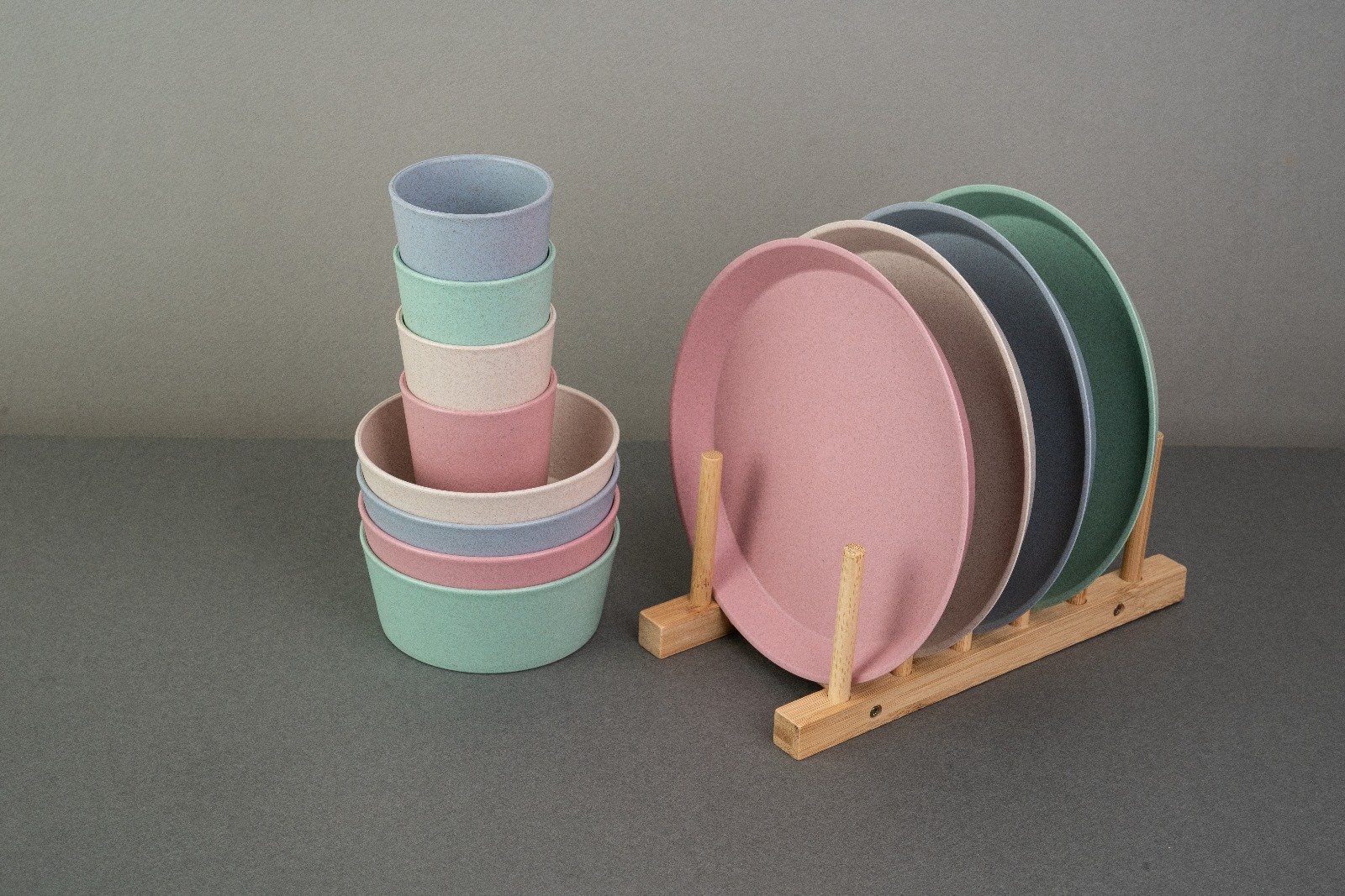 Colorful reusable tableware including plates and cups, arranged on a wooden stand.
