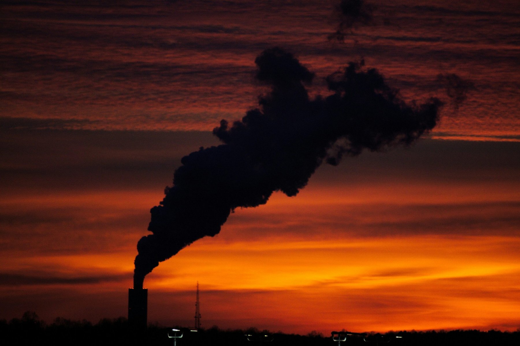 Black smoke rising from a smokestack against a vibrant sunset background.