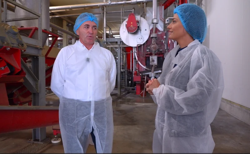 Doi oameni discută într-o unitate de producție de carne de pui, purtând echipament de protecție.